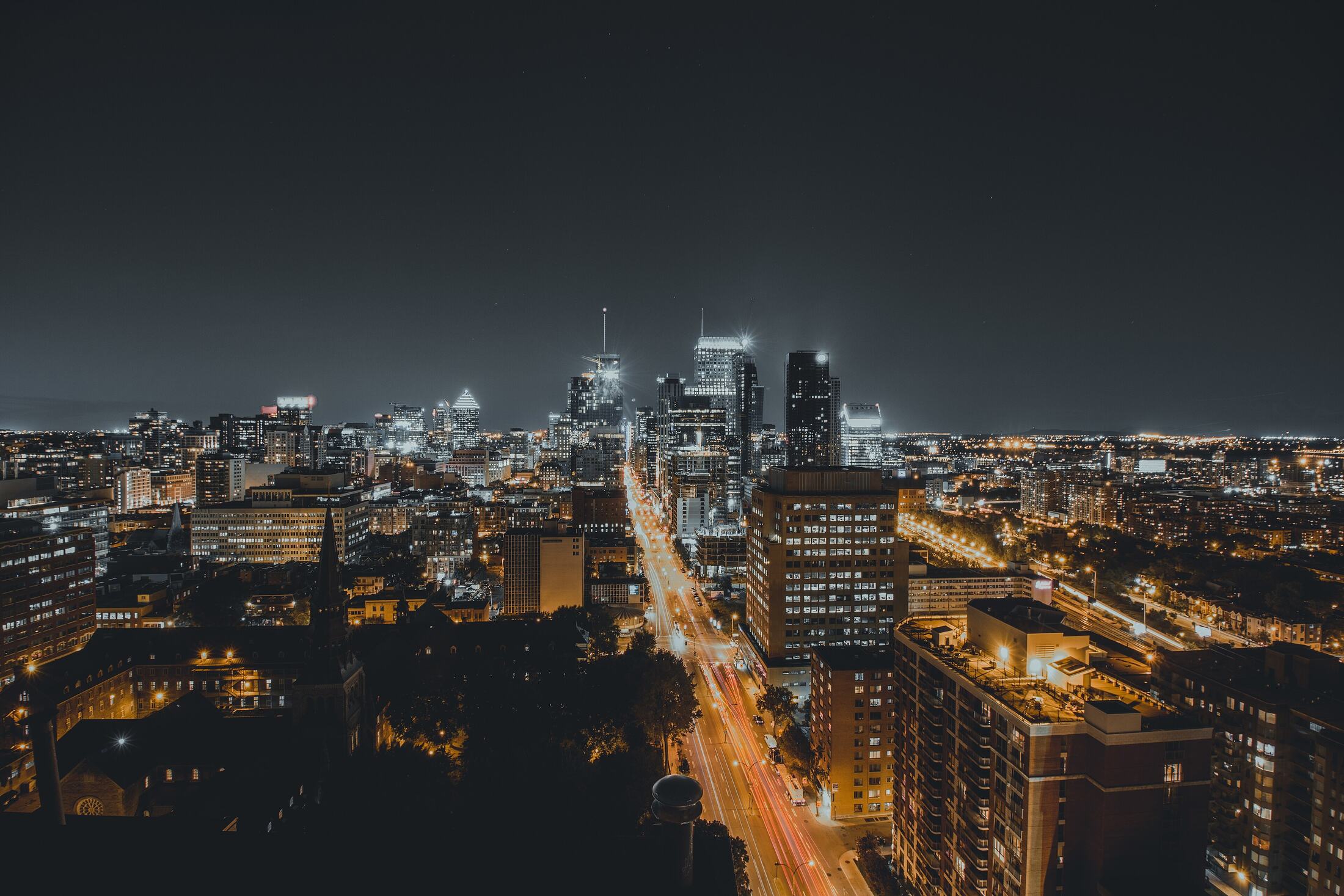 A city at night seen from above, with lit towers and a long avenue of traffic.
